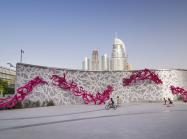 eL Seed, Declaration. Courtesy of the artist. a large installation piece in context—with city visible in the distance and children riding on bikes in front. 