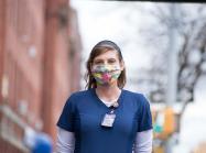 Catherine “Cat” Carnes, a registered nurse, stands on the street wearing a mask and scrubs