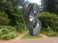 a photo of a large metal sculpture in a twisted organic form in a lush garden setting