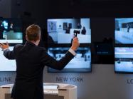 an auctioneer with a gavel stands in front of three large computer screens