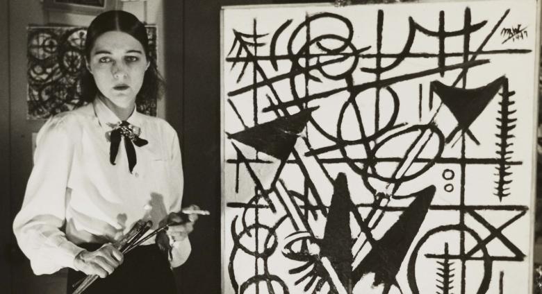 artist stands next to her work, brushes in hand but nicely dressed. Her features and clothes are as strikingly monochrome as her artwork. 