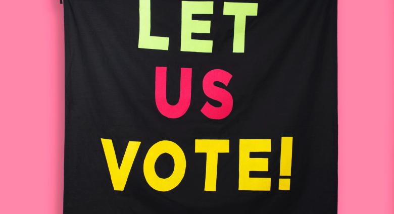 black banner that reads "let us vote" hanging on a pink banner