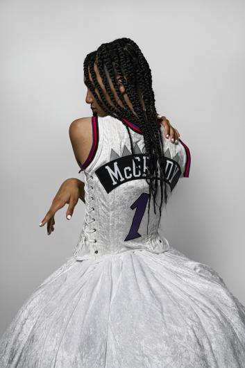 Woman stands in ballgown made from part of a basketball jersey. Her back is to the viewer.